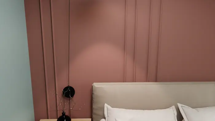 Bedroom with a dusty-pink panelled wall and a slim black pendant beside the bed.
