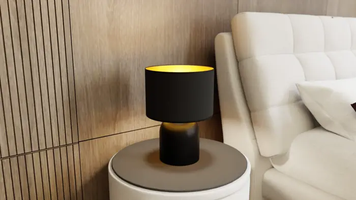 Table lamp with a black shade on a bedside table next to a pale upholstered bed.