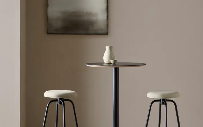 Dining corner with a slim round table and upholstered stools against a warm plaster wall.